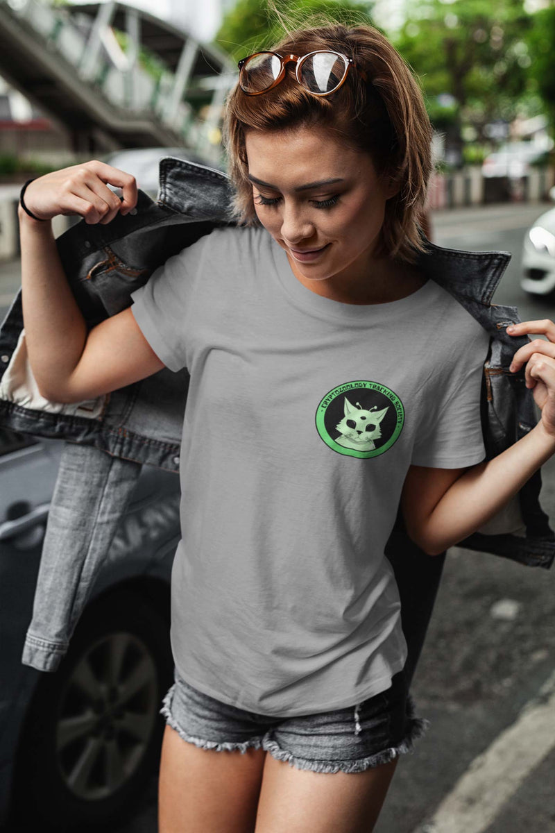 woman in light gray short sleeve shirt with cryptozoology alien cat logo printed on the left crest. 